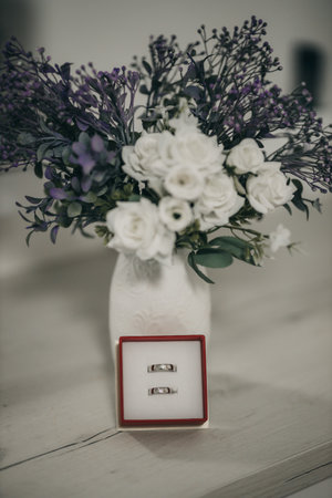 A vertical shot of a red box with silver wedding rings near a vase with flowers