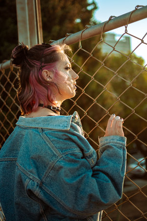 A vertical shot of a cool young Caucasian lady with pink hair, gothic style makeup and clothing