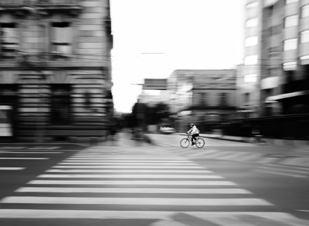 A grayscale blurred motion of a man riding a bike in a city