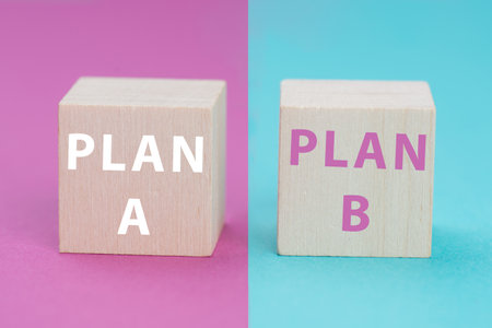 Plan A and B standing on wooden cubes, pink and blue colored background, options of possibilitiesの写真素材