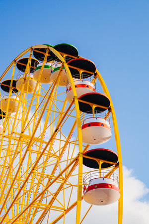 A vertical shot of a yellow amusement park wheel under a blue sky
