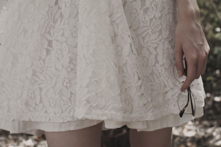 A lady with a white dress holding her optical glasses in the parkの写真素材