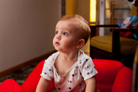 A portrait of a cute little Caucasian kid sitting on a red couch.の写真素材