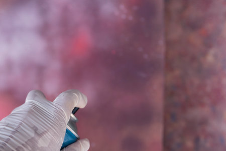 A hand wearing a latex glove and spraying blue paint from a graffiti canの写真素材