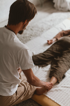A young Caucasian bearded masseur and a woman doing Thai yoga massage exercises on a mat at homeの写真素材