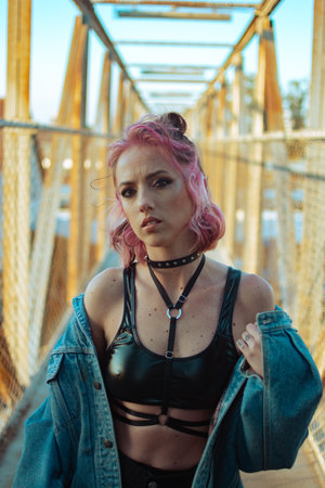 A vertical shot of a cool white lady with pink hair, gothic style makeup, clothing, and accessories