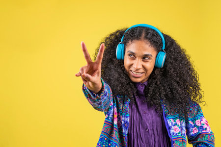 A young Hispanic female with curly hair listening to music with headphones on a yellow background