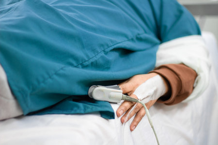 A closeup on a hand of a patient with an oximeter on the finger while lying on a hospital bedの写真素材