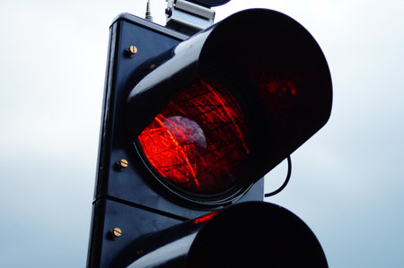 Detail of a red light of a construction site traffic light. The reflection shows a blue-white sky...