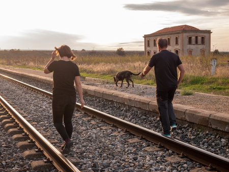 An adult couple walking with their dog on a railroad during sunset