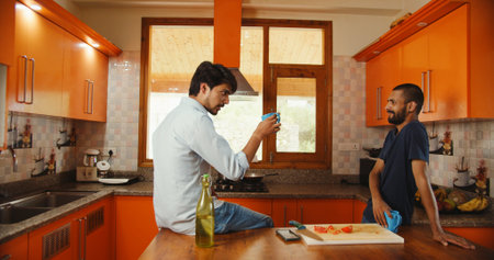Two Indian friends talking while drinking coffee in the kitchenの写真素材