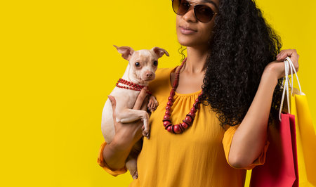 A cute Hispanic woman with a dog and shopping bags on a yellow backgroundの写真素材