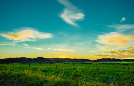 A beautiful pasture field below the mountain against a cloudy sunset skyの写真素材