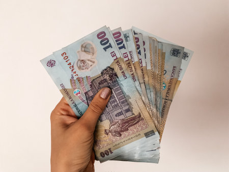 A closeup of a person holding cash Romanian leu against a beige background