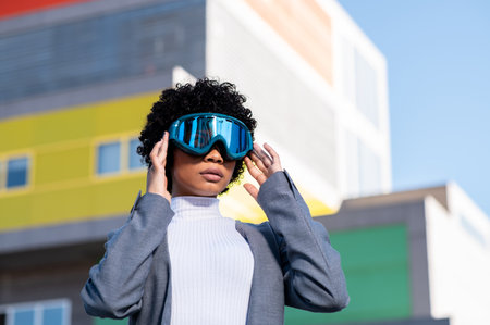 A cool young African American lady with curly hair wearing ski goggles in a residential areaの写真素材