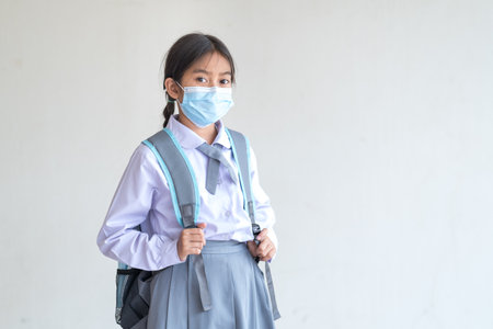 A cute beautiful Southeast Asian school girl with braids in a uniform wearing a mask due to the...