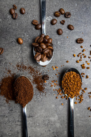 A top view of stainless steel spoons with whole bean coffee and ground coffee beans