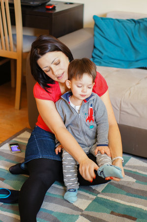 A vertical shot of a young caucasian mother dressing her baby son