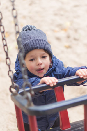 A vertical shot of a cute little caucasian boy playing with a swing
