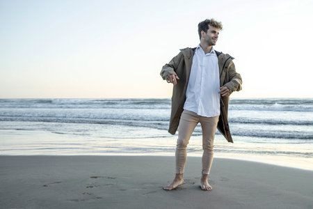 A young attractive blue-eyed Caucasian man with curly hair posing at a beach