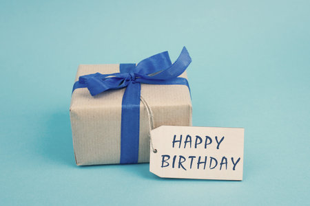 Small gift box with a blue ribbon and  a tag with the text happy birthdayの写真素材
