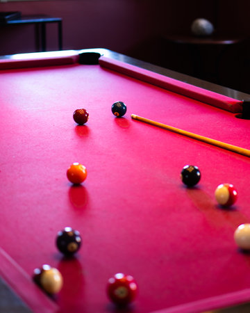 A vertical shot of a red billiard table with balls and stick