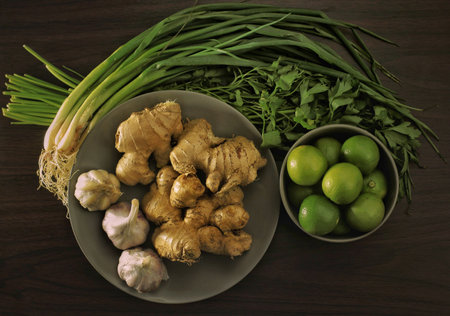 A top view of garlic ginger lime scallion and parsley in plate and bowl with a wooden backgroundの写真素材