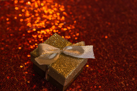 A closeup of a beautiful golden gift box on red glittery backgroundの写真素材