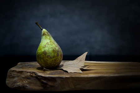A closeup of a delicious green pear with brown spots on it on a wooden surfaceの写真素材
