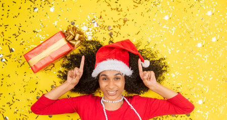 A cute Hispanic woman with a Christmas dress and boxes on a yellow backgroundの写真素材