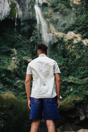 A vertical shot of a guy standing in front of a waterfallの写真素材
