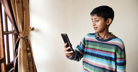 A Closeup of a south Asian young boy with a colorful striped pullover playing with a phone