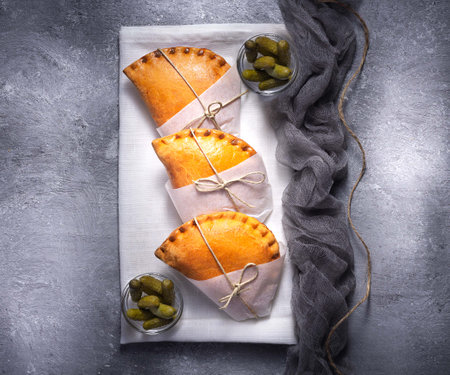 A top view of freshly baked empanadas on a white cloth served with picklesの写真素材