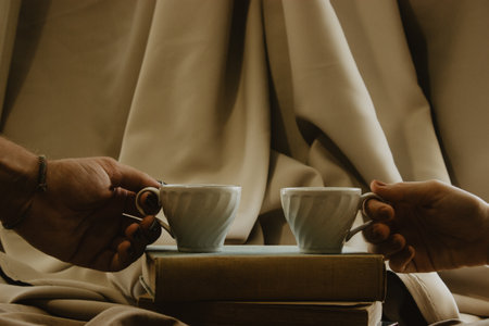 A couple holding a cup of coffee on piled old books and beige fabric backgrounndの写真素材