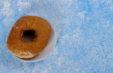 A top view closeup of a fresh doughnut on a small white plate with a light blue texture backgroundの写真素材