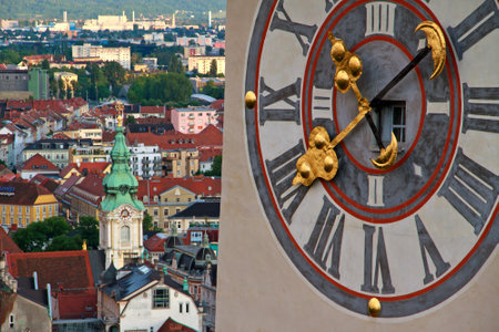 Landmark clocktower in Graz with huge clock and the citycentre in the backの写真素材