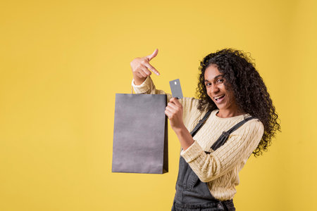 A young Hispanic female holding a shopping bag and pointing to her credit cardの写真素材