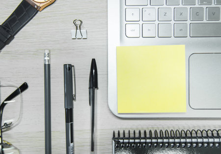 A working desk with a wristwatch, glasses, pens, notebook, clip, and laptop - work from home conceptの写真素材