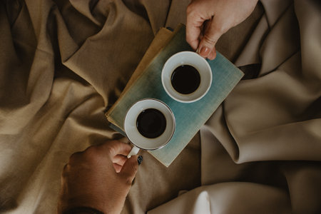 A couple holding a cup of coffee on piled old books and beige fabric backgroundの写真素材