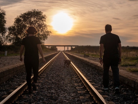 An adult couple walking with their dog on a railroad during sunsetの写真素材
