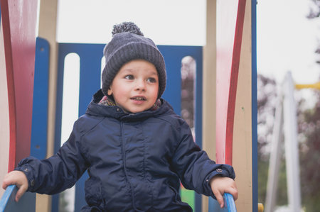 A portrait of a cheerful Caucasian boy on a slide in the playground