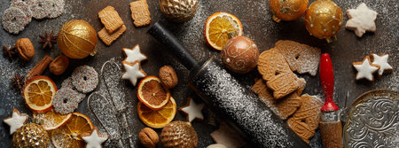 A top view of Christmas biscuits, baking tools, baubles, dry oranges, and nuts on the tableの写真素材