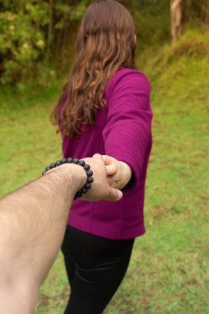 A vertical shot of a Hispanic female in nature holding hands with her romantic partnerの写真素材