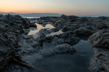 A rocky shore surrounded by the sea and hills during the sunrise in the morningの写真素材