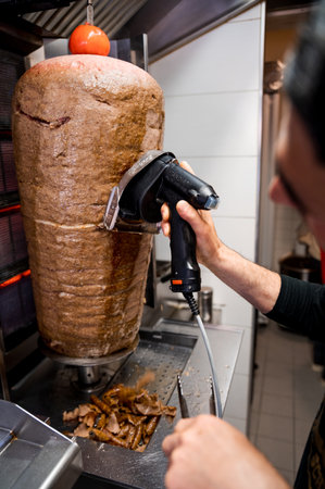 A chef carving meat from shawarma griller using akebab slicerの写真素材