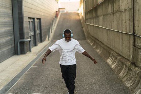 A young cool black male in a street style outfit dancing with headphones outdoors