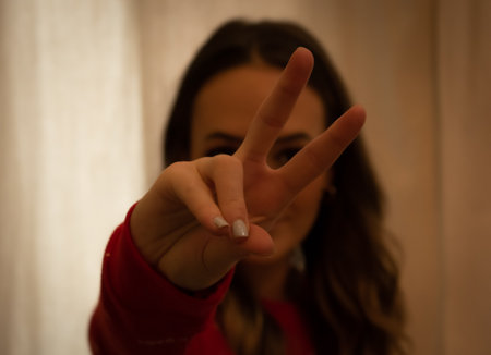 A portrait of a young brunette girl showing the peace sign at homeの写真素材