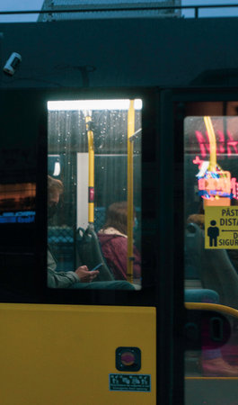 A closeup of a Person with a facemask sitting in the bus looking at the phone on a rainy dayの写真素材