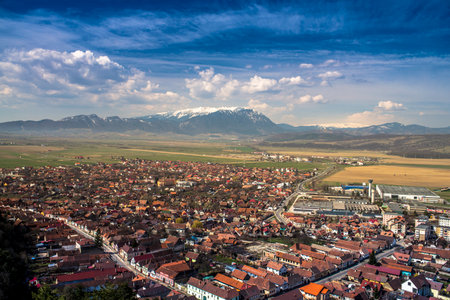 A cityscape of Rasnow surrounded by hills under a blue cloudy sky in Romania