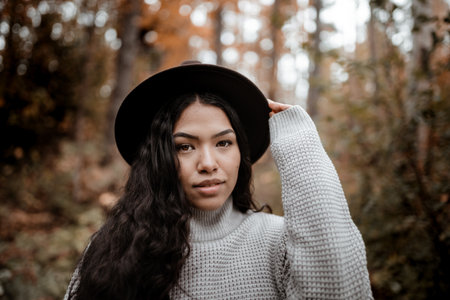 A portrait of a young beautiful Hispanic woman with an elegant outfit adjusting her brown fedora hat